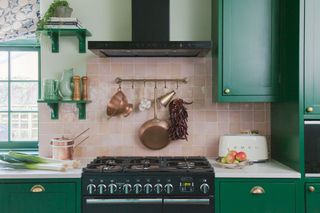 kitchen with green cupboards range cooker and pink tiles behind