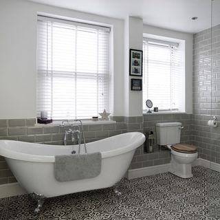 bathroom with white and grey brick wall bathtub window and designed flooring