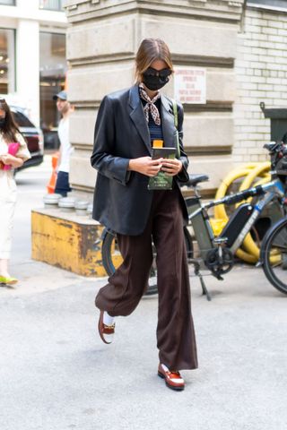 Kaia Gerber wearing a black leather blazer with brown trousers and loafers