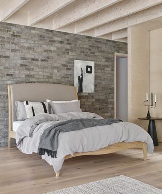 bedroom with brick wall behind bed and grey and neutral colour scheme