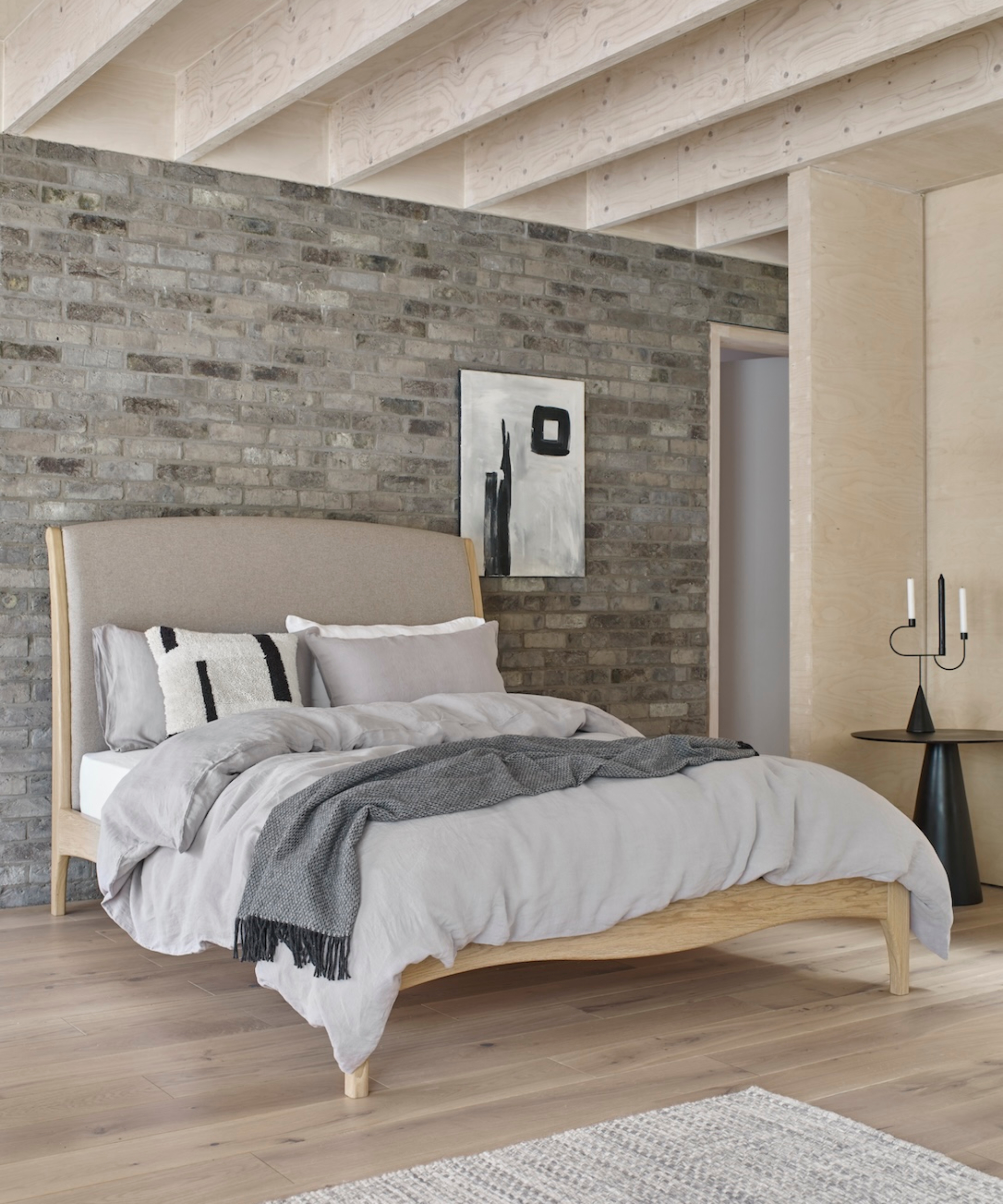 bedroom with brick wall behind bed and grey and neutral colour scheme