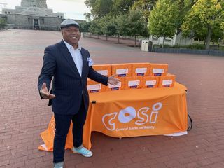 COSI President Dr. Frederic Bertley standing with a table of American Innovation Learning Lunchbox STEAM Kits