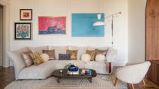Image of a white living room with a beige sofa and beige rug. There is a four-picture gallery wall above the sofa and a small wooden coffee table in front of the sofa.