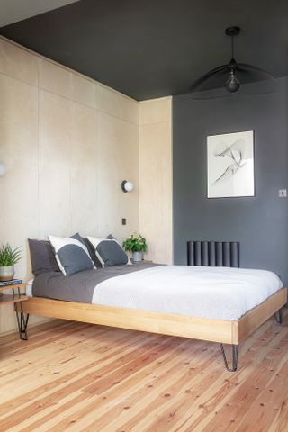 Black bedroom with black walls and black ceiling, plywood wall against bed, statement ceiling light and monochrome wall art