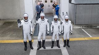 four astronauts in white spacesuits wave to cameras