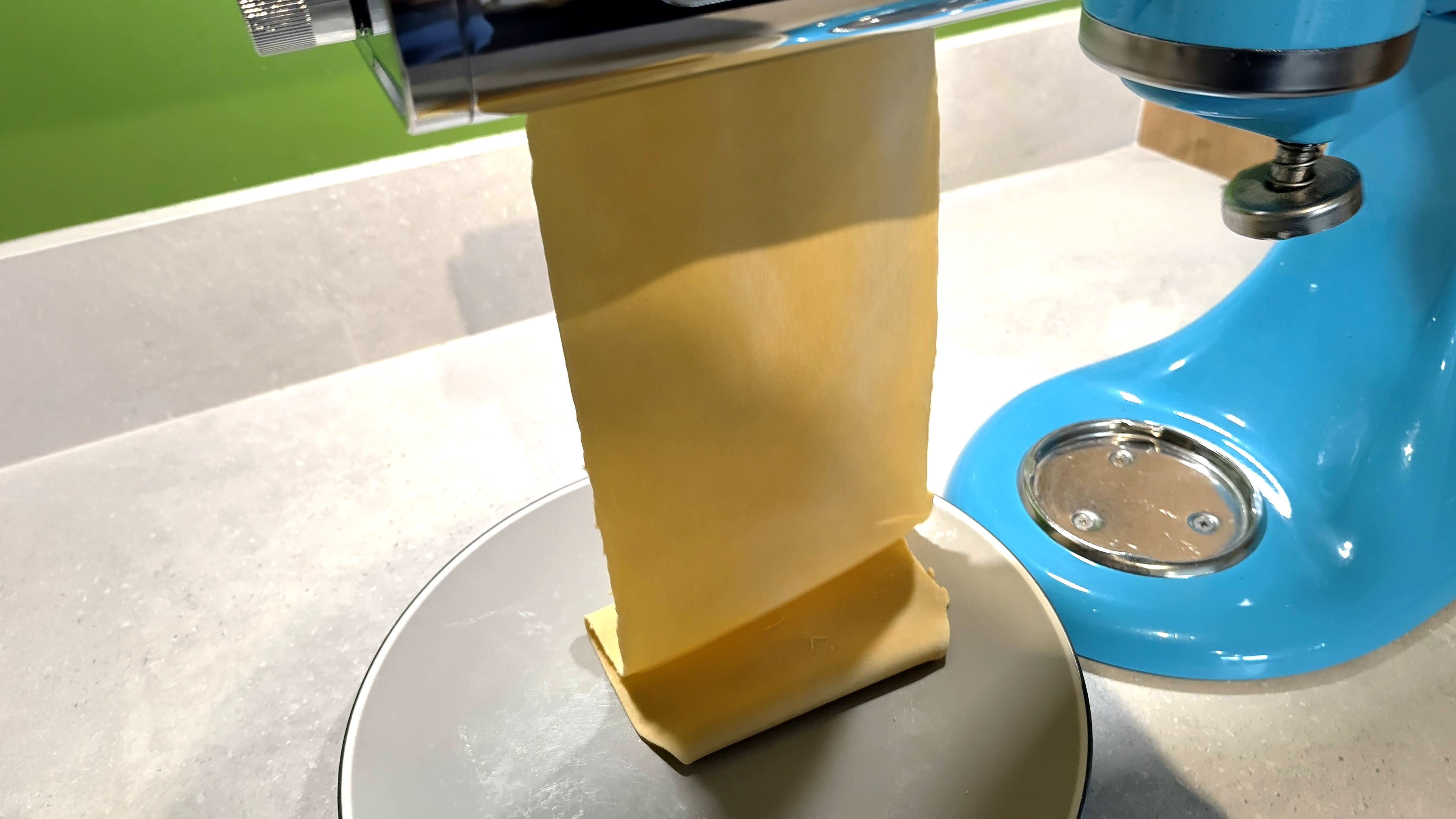 KitchenAid stand mixer with pasta roller attachment rolling a sheet of pasta
