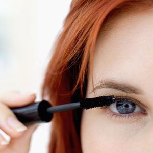 red haired female applying mascara