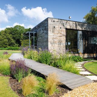 a timber clad mobile home in the New Forest with a path leading to the gravel driveway and a garden filled with plants