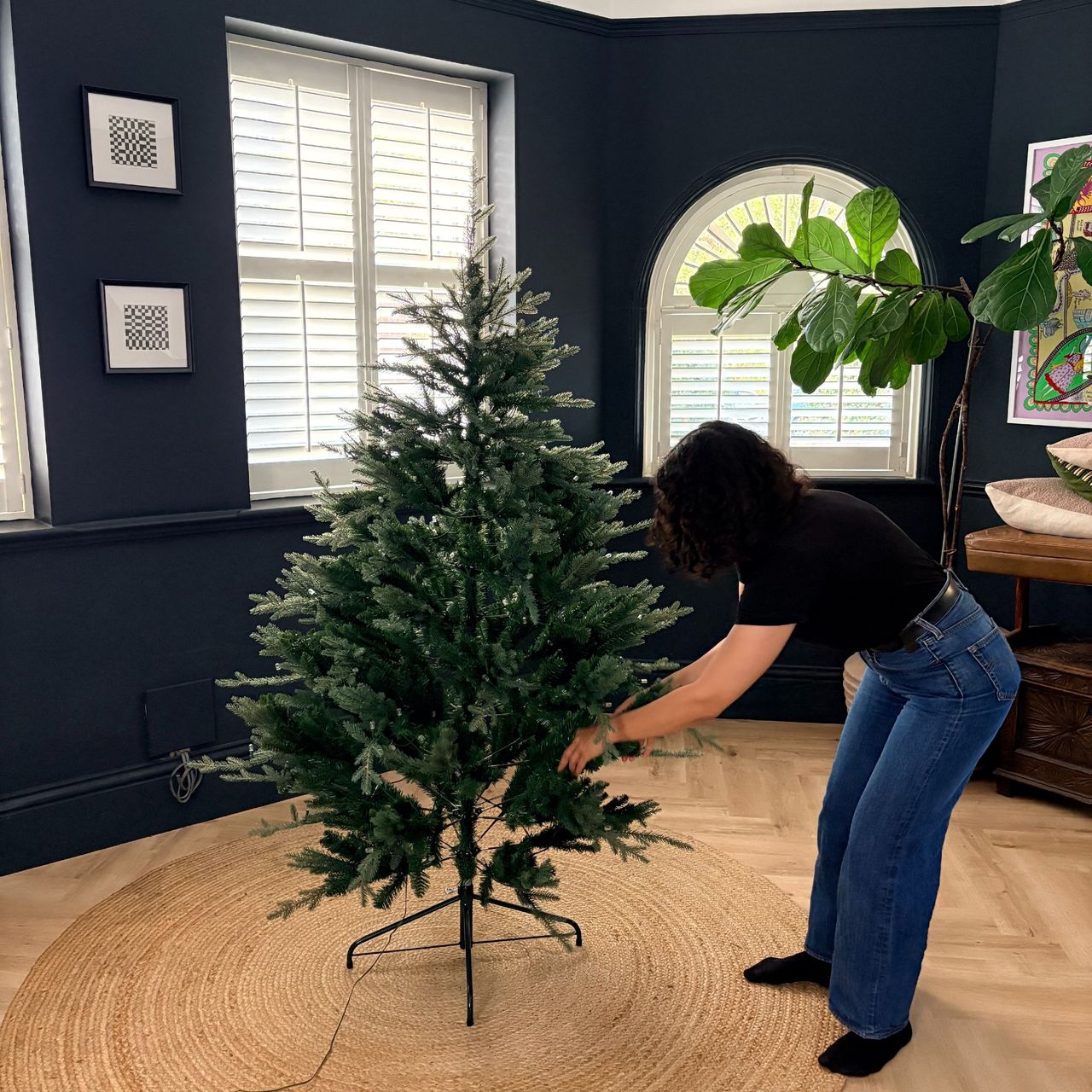 Sara Hesikova fluffing out the branches of an artificial Christmas tree in a black-painted Christmas tree