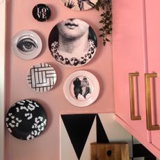A pink cupboard with a pink-painted wall displaying a decorative plate gallery wall