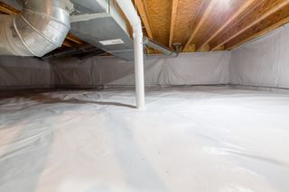 Crawl space fully encapsulated with thermoregulatory blankets and dimple board. Radon mitigation system pipes visible. Basement location for energy saving home improvement concept.