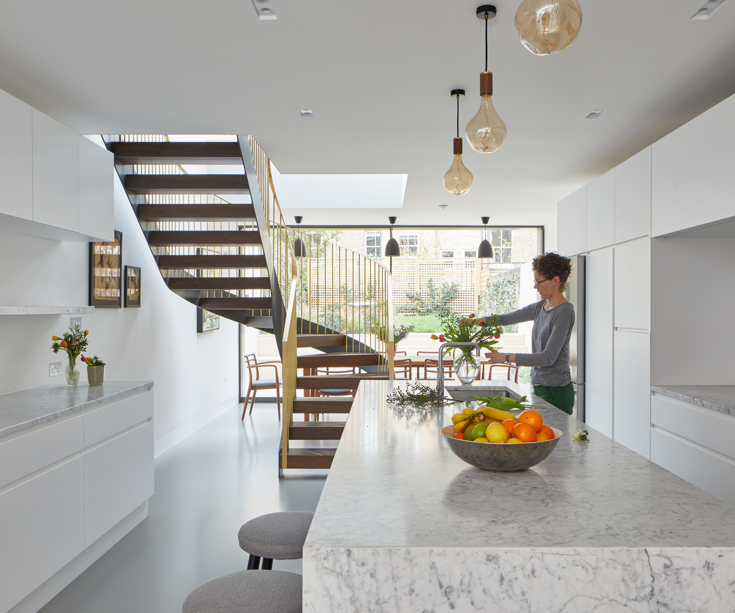 open plan modern kitchen with grey marble island and spiral staircase leading opening into double height section at end of room