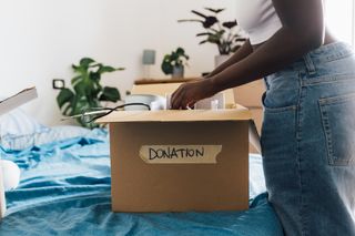 A woman packing away her belongings into a cardboard box with the word 'Donation' on the side.