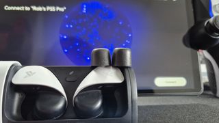 Two earbud tips sitting on top of the PlayStation Pulse Explore earbuds case in front of a PlayStation Portal on a black surface