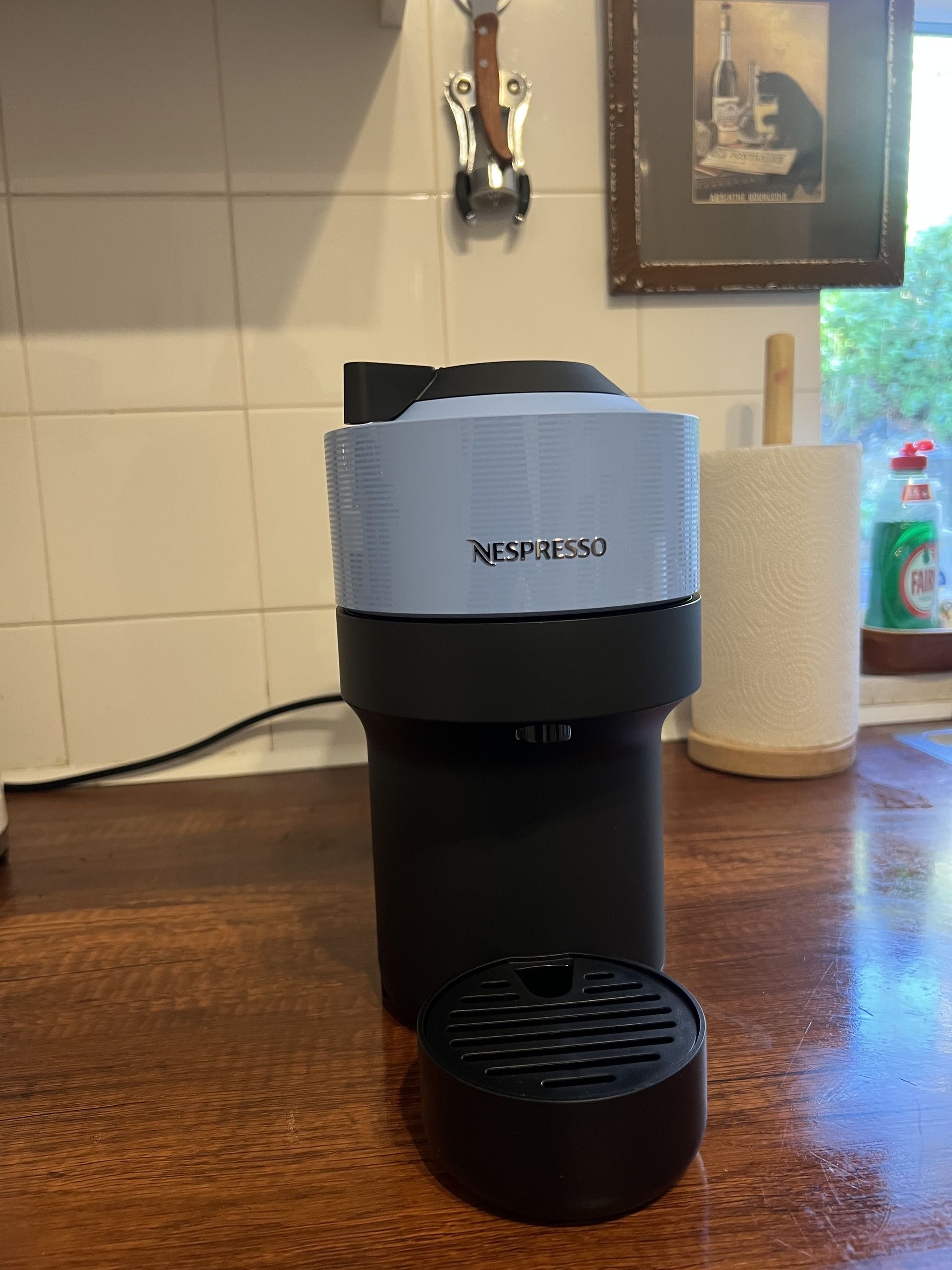 Image of a light blue and black Nespresso Vertuo Pop machine on a wooden kitchen countertop. 