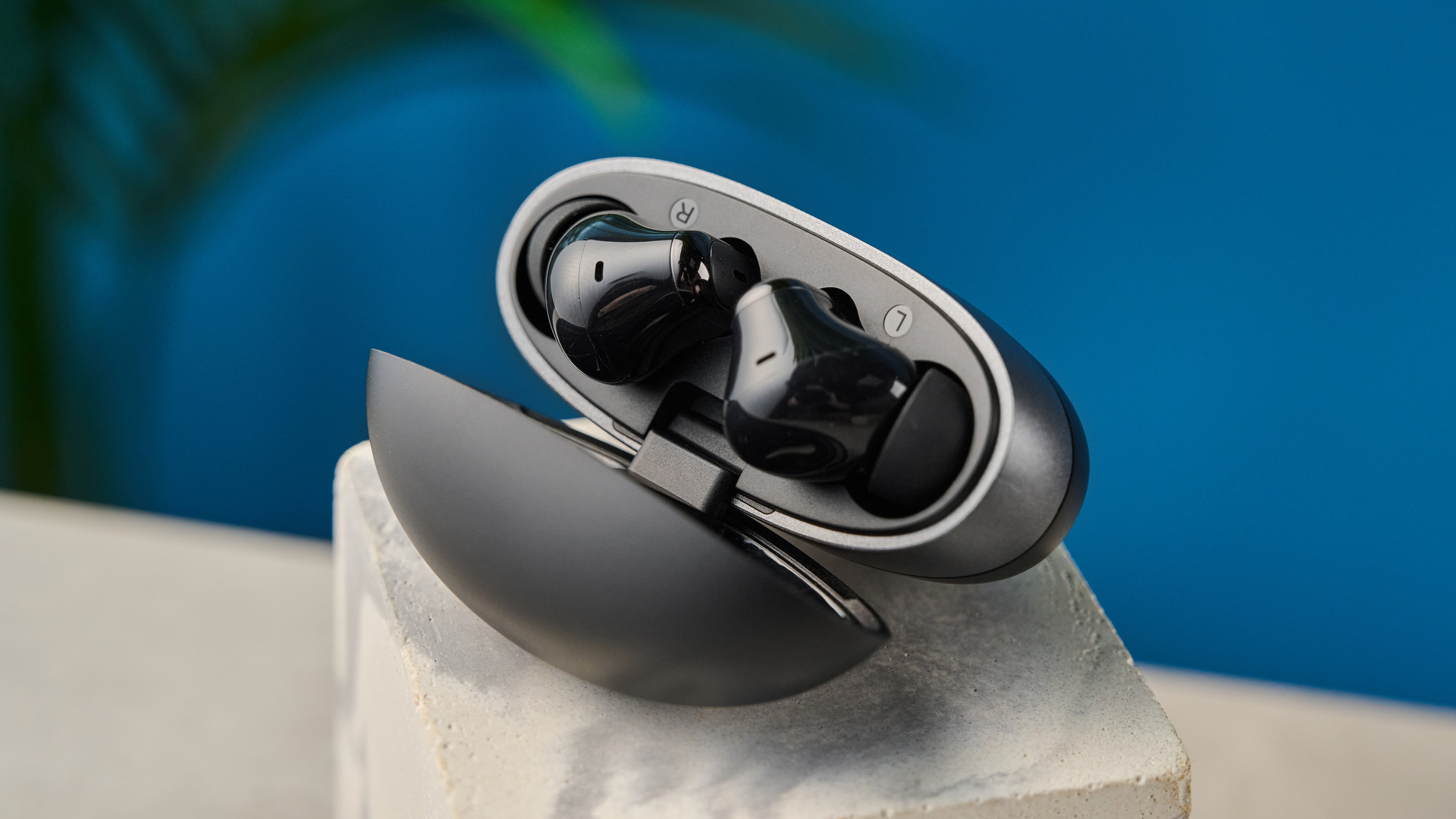 Tribit FlyBuds C3 in black photographed on a blue background with leaves