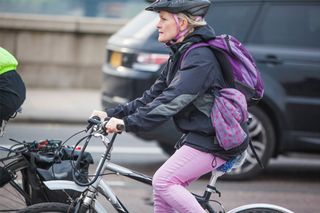 This is an image of a woman's commuting by hybrid bike. She has a lock on her handle bars and a purple rucksack on her back
