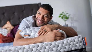 A man with closely cut black hair smiles while lying on his stomach on the Layla Kapok Pillow