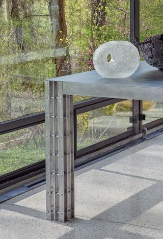 Metal table on terrazzo floor near the window with glass sculpture