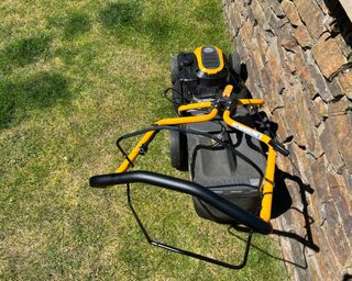 petrol mower on a lawn next to a stone wall