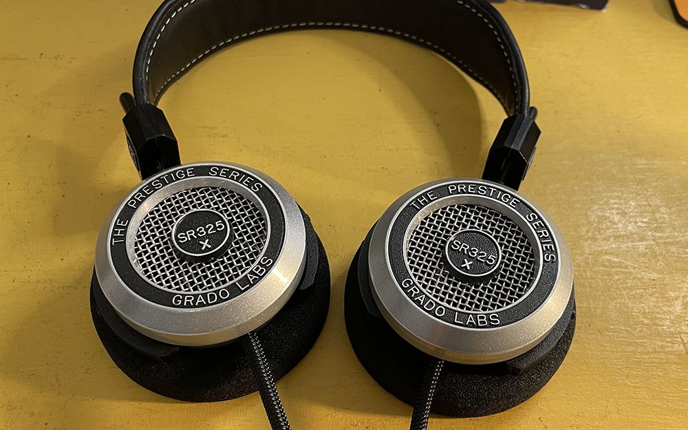 The Grado SR325x on-ear headphones lying earcups-down on a yellow surface, shot straight-on.