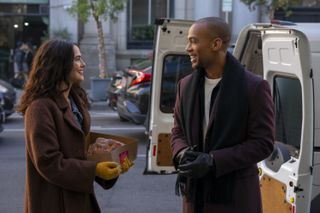 a woman (zoey deutch) holds a box of pastries and smiles with a man (kendrick sampson) as they stand in front of an open van, in the prime video rom-com 'something from tiffany's'