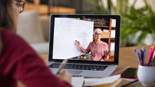 Woman sat in front of laptop, which shows woman pointing at whiteboard