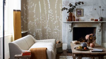 A living room with a cream sofa and two different wallpapers, one surrounding the fireplace and a botanical beige design in an alcove