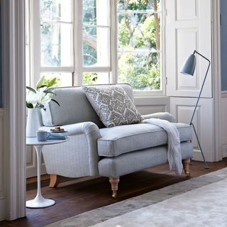 blue loveseat situated in the alcove of a bay window, with a blue coffee table one side and a blue floor lamp the other side