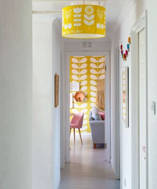 hallway attached to living room with wooden floor and white and yellow wall and yellow ceiling lamshade