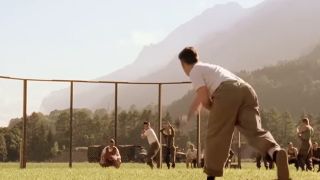 Cast members playing baseball in Band of Brothers with mountains behind them