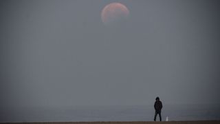 A man takes a walk during the total lunar eclipse from Santa Monica Beach in California on May 26, 2021. Totality, when the Flower Moon turned red, last just over 14 minutes.