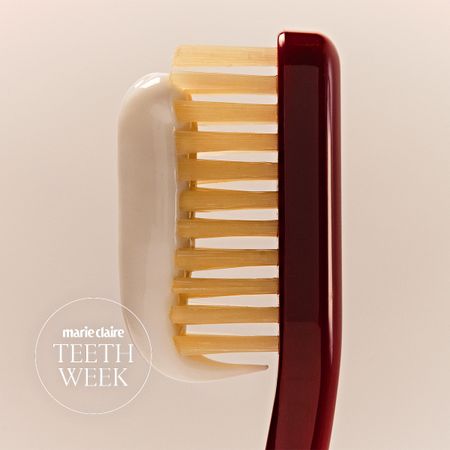 white toothpaste on a burgundy toothbrush on a cream background