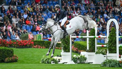 Harry Charles and his grey mare clear a large oxer of mainly white poles, with just a small green and red stripe at each end, during the speed leg of the showjumping World Champions in Aachen