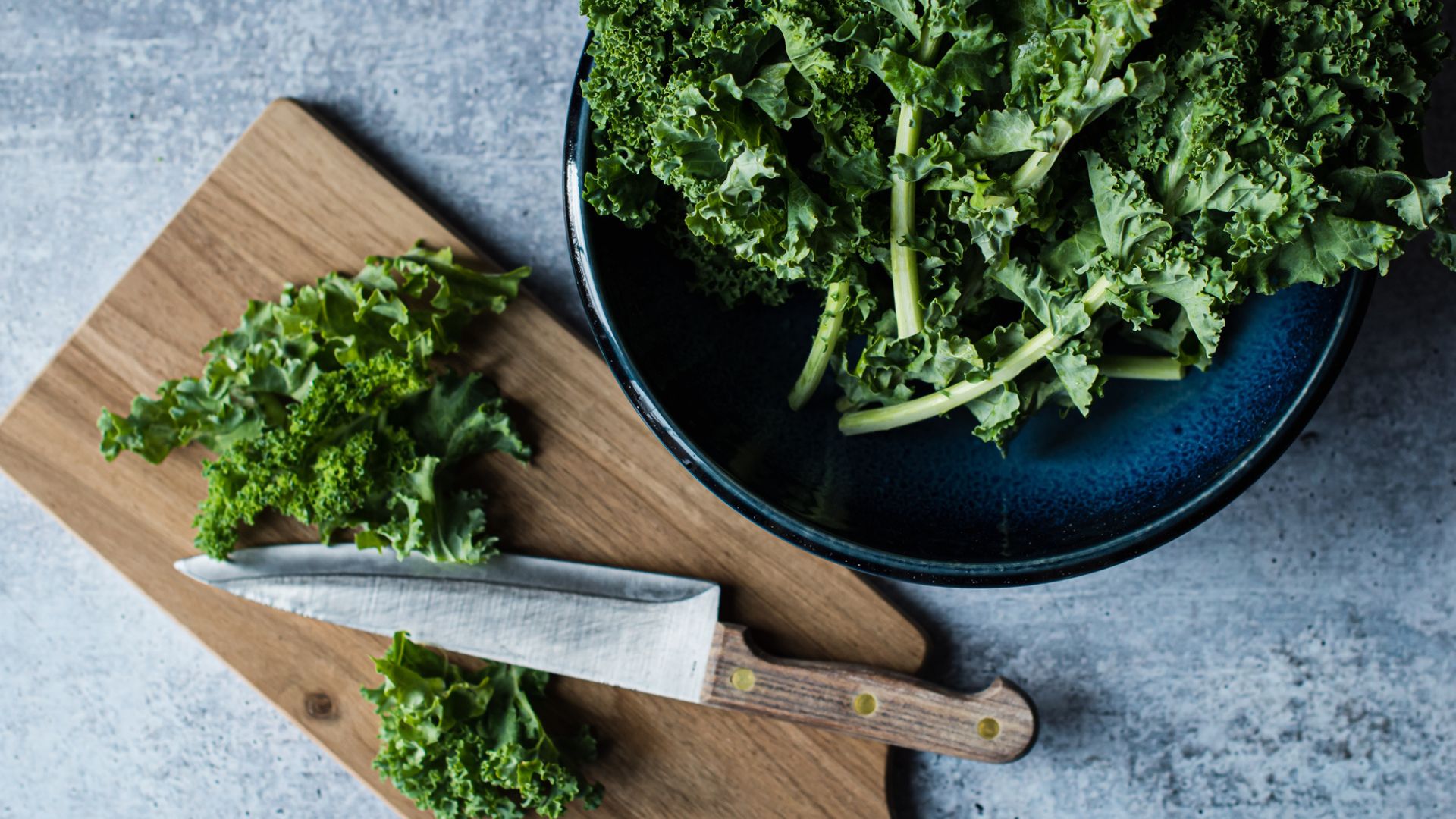 Bowl of crunchy kale next to wooden chopping board and steel knife