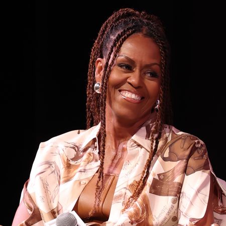 Michelle Obama with twists in her hair. She is wearing silver earrings and smiling 