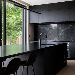 Black kitchen units, countertop, and island next to large window