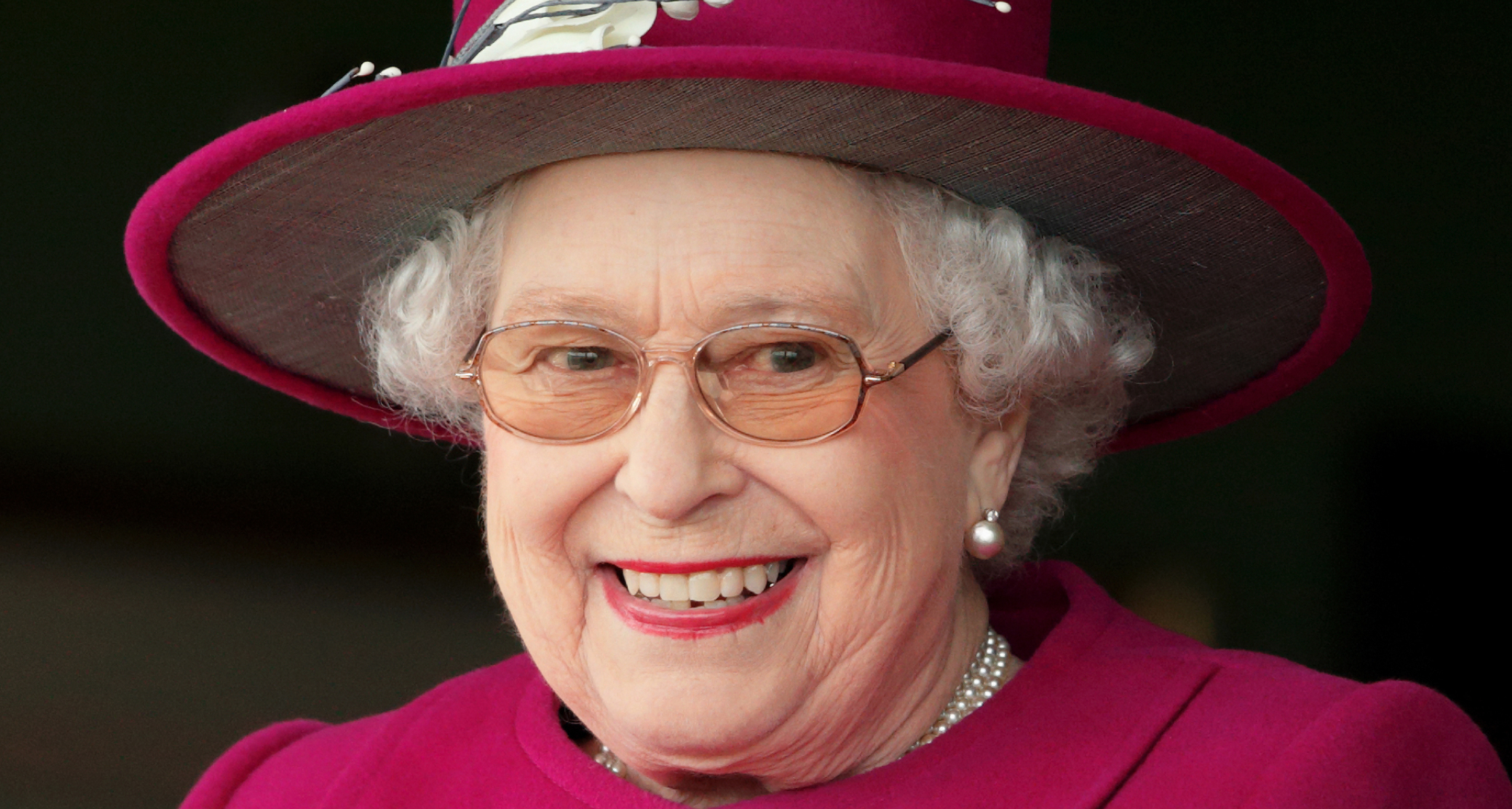 Queen Elizabeth wearing a magenta hat and coat looking excited