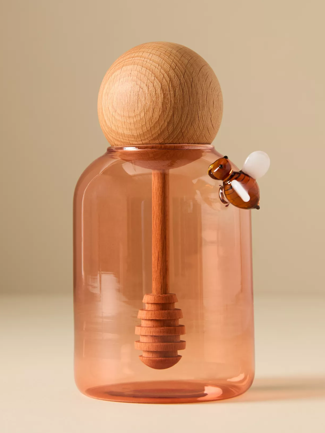 An amber glass honey pot with a wooden wooden dipper and a glass bee flourish from Anthropologie