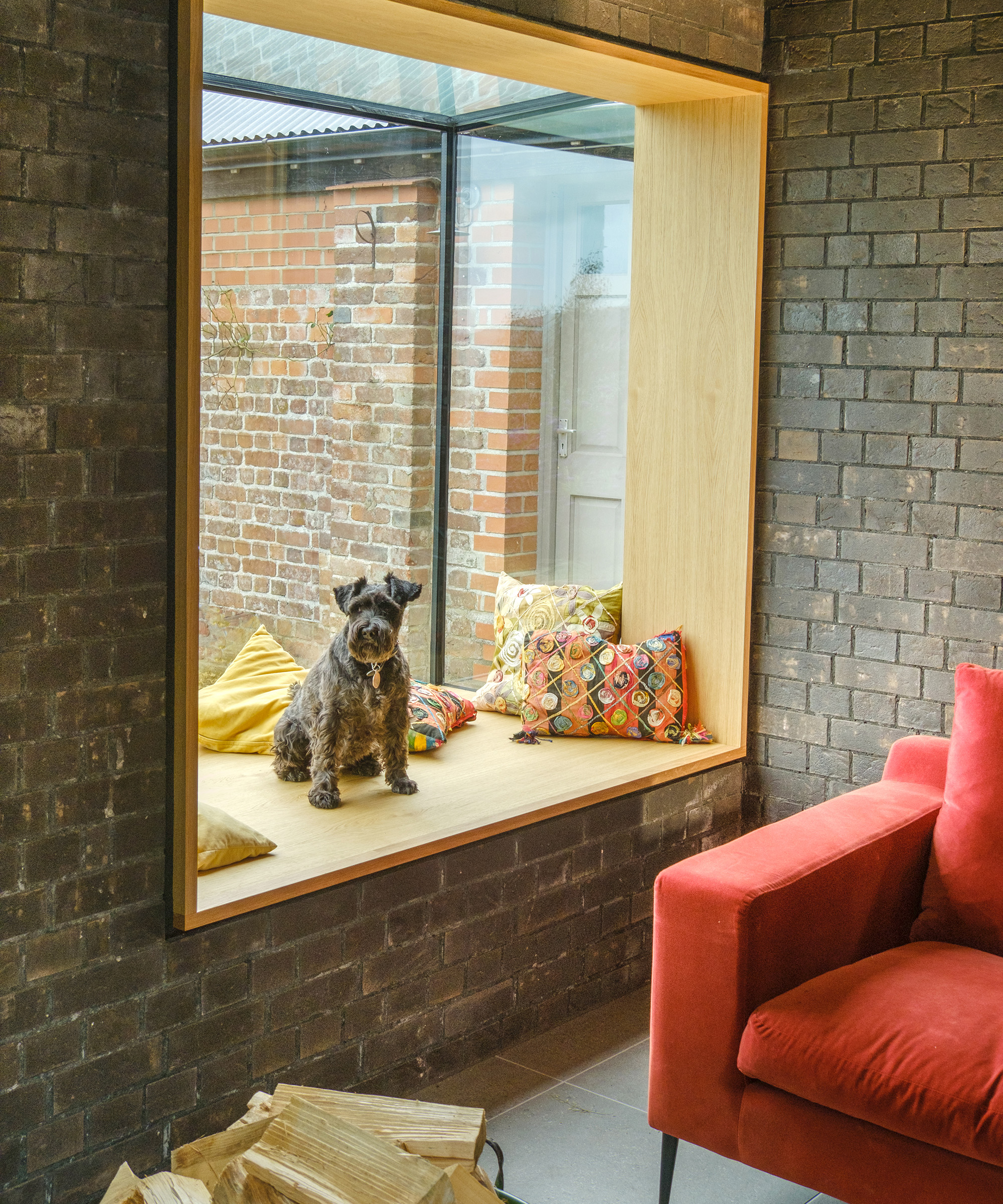 A picture window with built in window seat with small dog seated there. The walls around are exposed bricks
