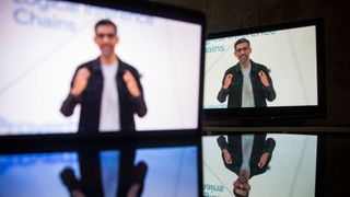 Google CEO Sundar Pichai shown on two screens, with one out of focus and the other in focus, reflected on glass in a dark room