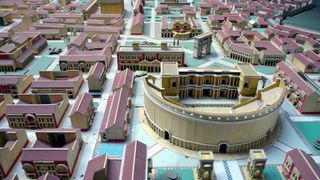 We see a virtual model of a Roman city, with red-roofed buildings and an amphitheater.