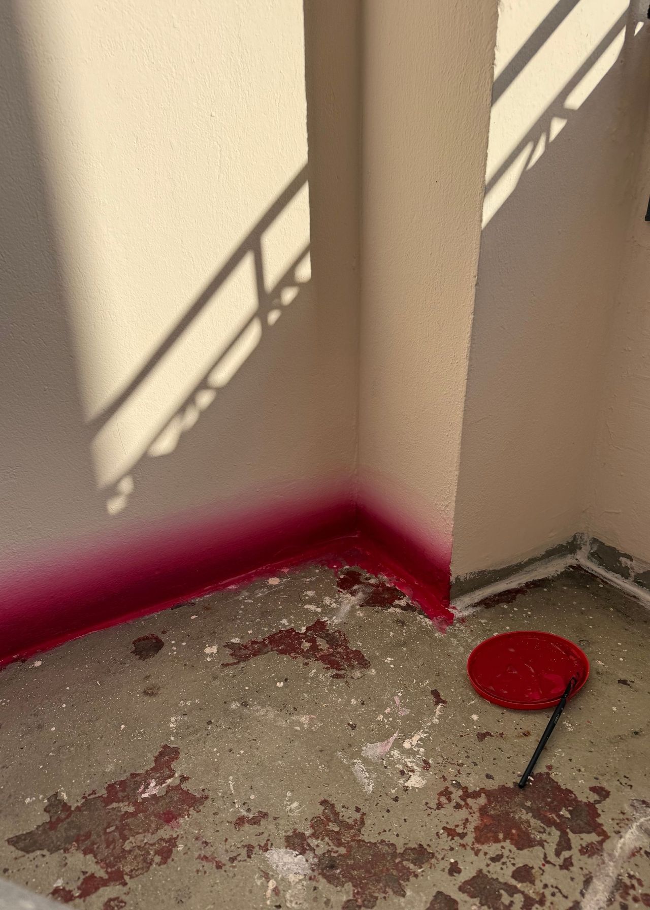 Image of a white balcony with unfinished flooring and half of the lower wall painted in a red and pink gradient.