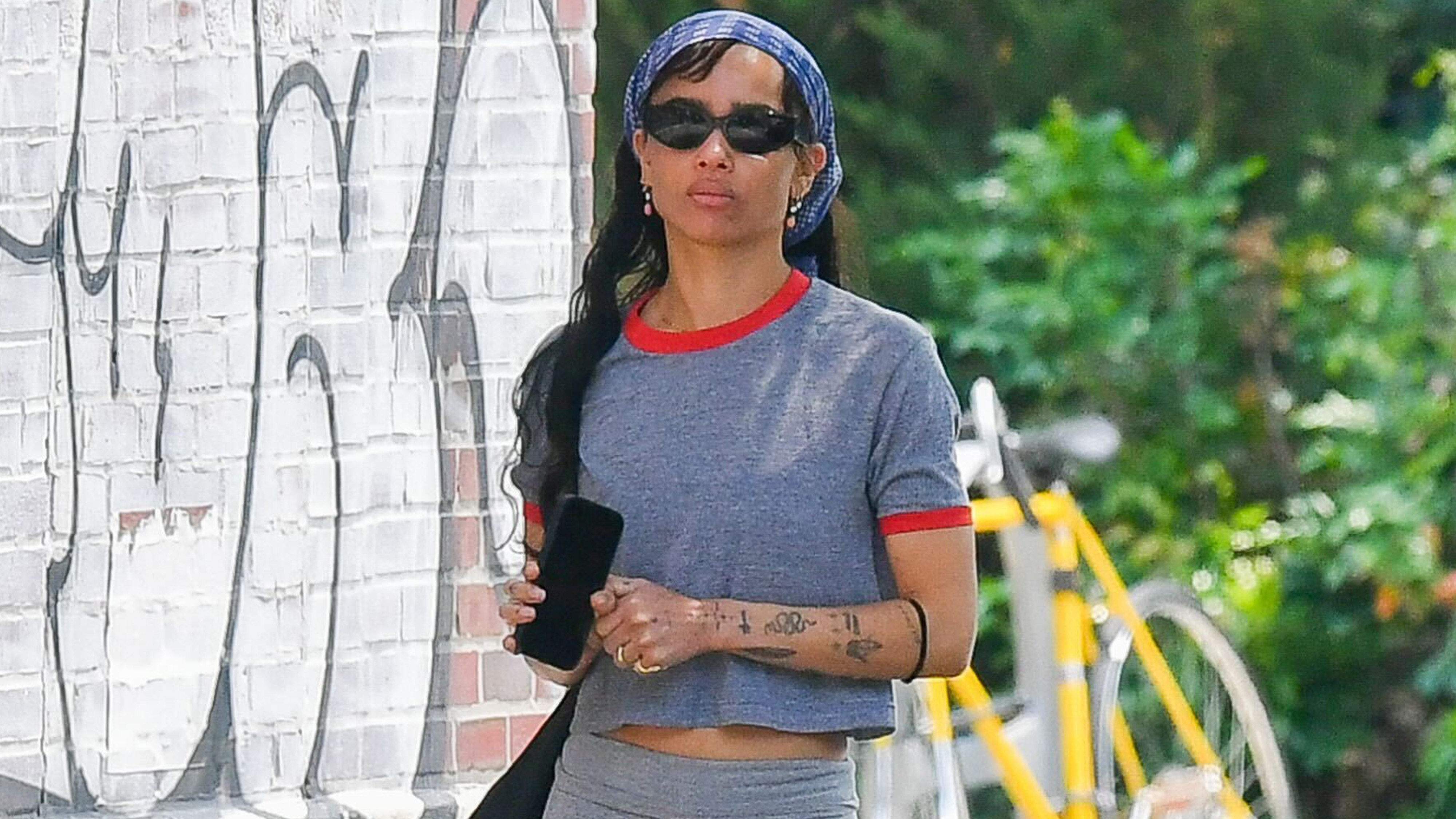 Zoe wears a bandana, gray t-shirt, and gray bike shorts with red sandals.
