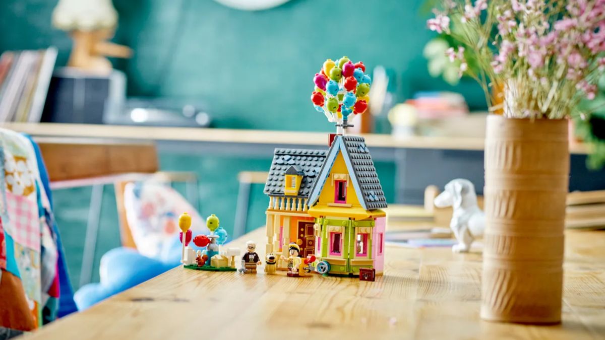 The fully-constructed Lego &#039;Up&#039; House on a wooden table, in a colorful setting with flowers and patchwork blankets