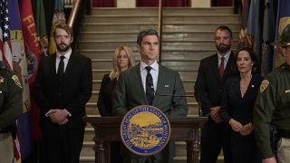 Attorney General Jamie Dutton (Wes Bentley) looking serious in a suit and surrounded by his colleagues - including Governor Lynelle Perry (Wendy Moniz) - as he prepares to give a press conference in the concluding episodes of Yellowstone Season 5.