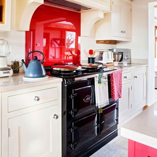 kitchen with red accent splashback and island, cream cupboards and black oven and stovetop