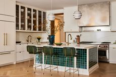 A view of a kitchen island covered in dark green tiles complete with three green stools