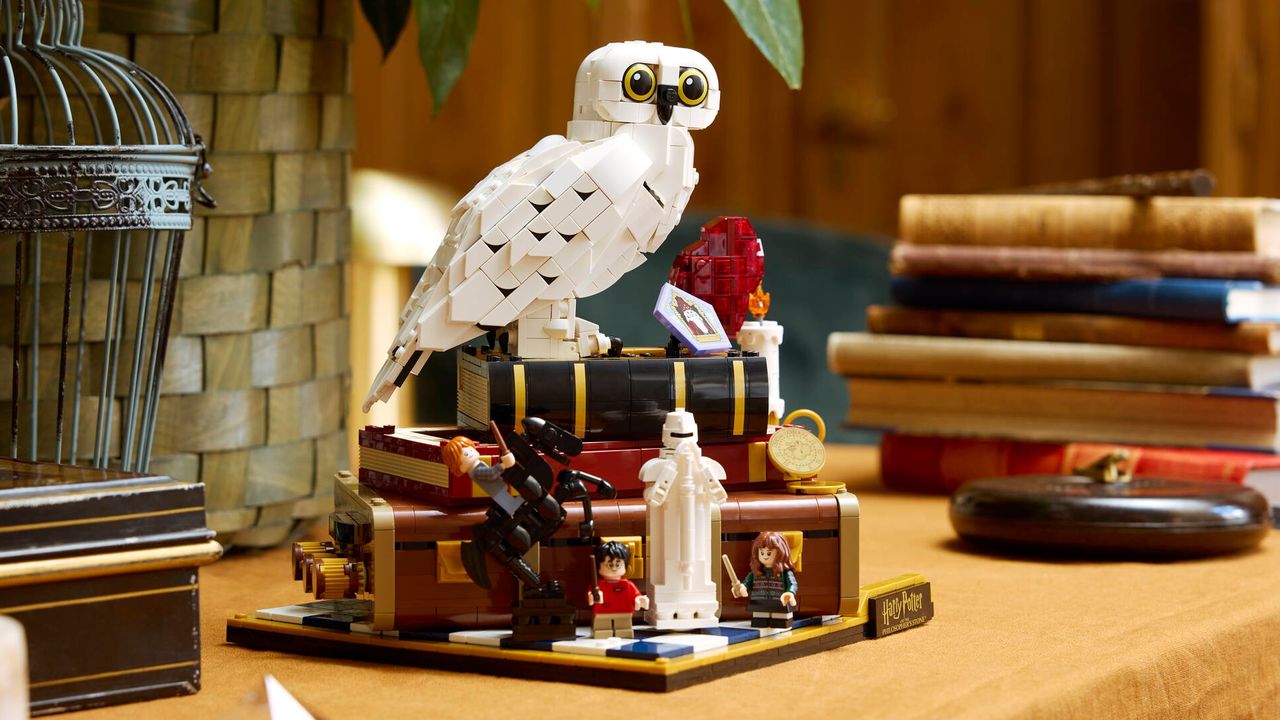 A Lego owl perches on a pile of books, beside actual books and a birdcage