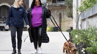 Canine Behaviourist and Training Manager Beth Bush-Kidd in a navy Battersea top stands next to Alison Hammond in a pink jumper and black coat as she walks spaniel Nelly on a lead in For the Love of Dogs with Alison Hammond.